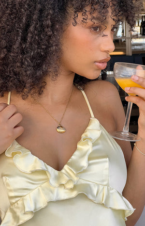 Girl wearing yellow frill dress and gold seashell necklace.