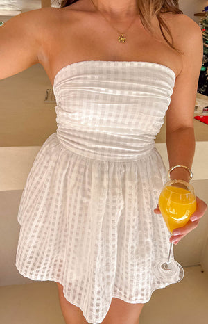 Girl wearing a white strapless mini dress and gold bow necklace holding a drink.