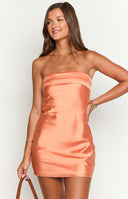 a blonde model poses in an orange strapless mini dress and a gold pendant necklace with a pink rose corsage on her wrist