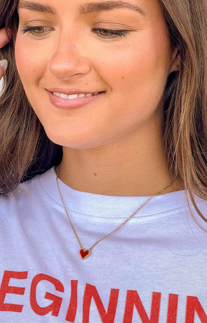 girl is wearing a small red heart-shaped pendant gold necklace 