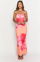 Brunette model is wearing an orange strapless maxi dress with pink floral patterns. She is holding a white handbag.