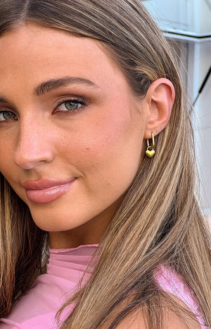 Blonde girl wearing pink mesh maxi dress and gold heart hoop earrings.