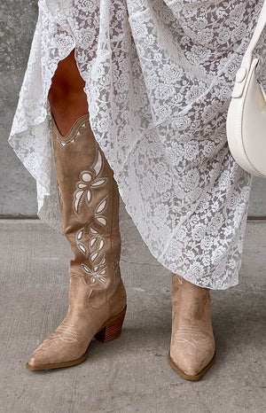 Girl wearing white lace maxi skirt and tan cowboy boots with white handbag.