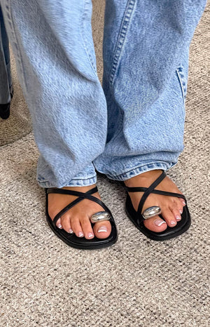 Girl wearing blue denim jeans and black sandals with silver details and french tip pedicure.