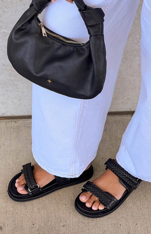 Girl wearing light blue denim jeans and black braided sandals and holding a black handbag.