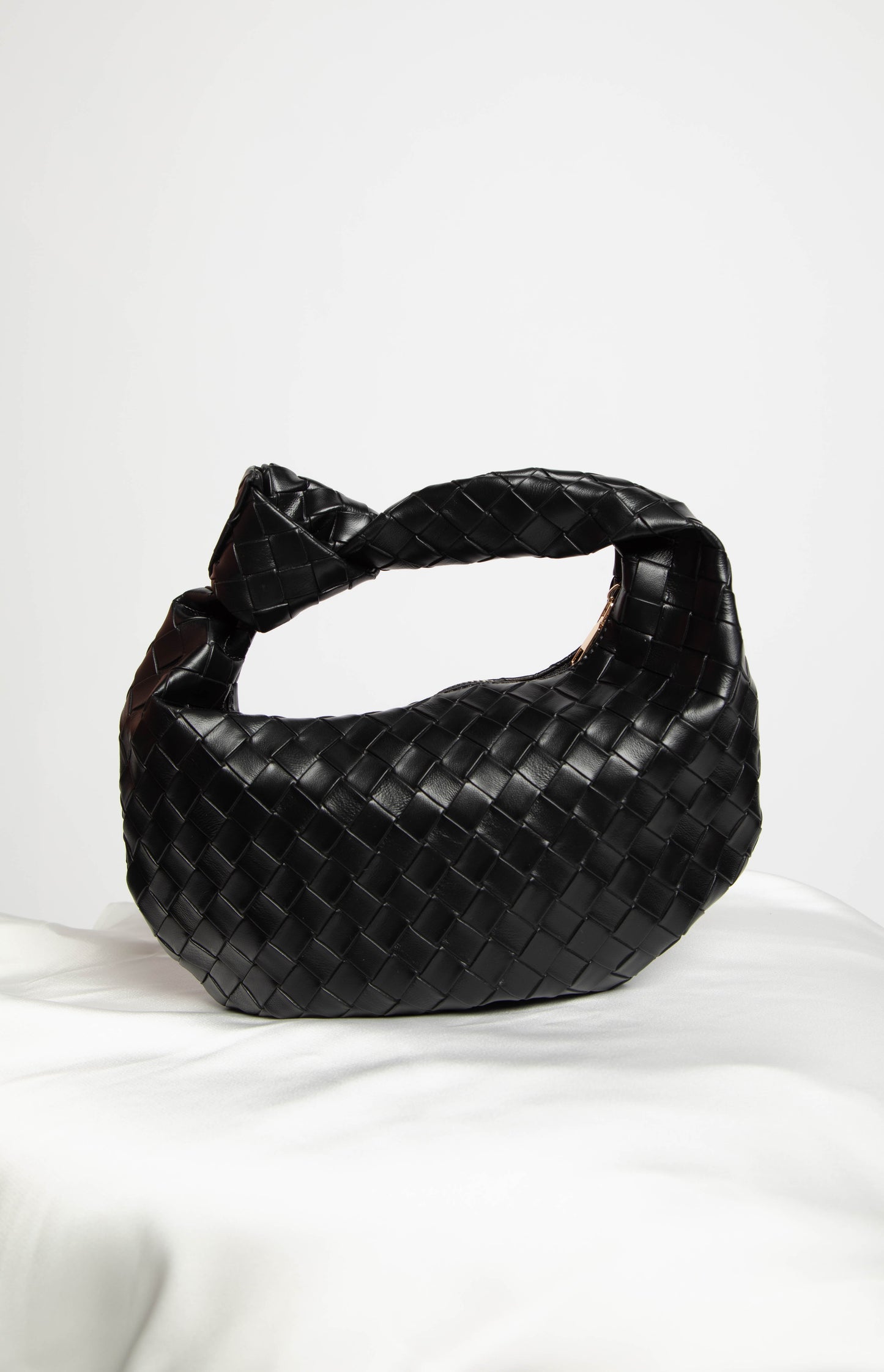 black woven leather bag with a tie in the strap on a white table