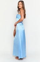 blonde model wearing a blue maxi dress with gold bracelets, a white hand bag and nude heels