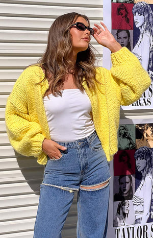 Girl in yellow knit cardigan holding her sunglasses and looking up at the sun.