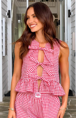 Model in red gingham top with bows with matching red gingham shorts looking to the side. 