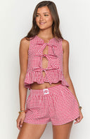 Model wearing a red gingham top with bow detailing down the front with matching shorts standing on a paved flooring. 