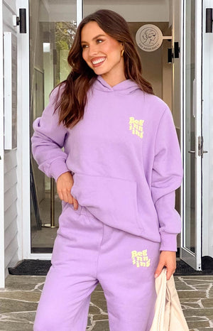 Model in purple tracksuit set, smiling and looking to the side. 