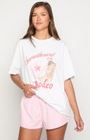 blonde girl wearing a rodeo inspired white graphic tee with an image of a cowboy hat and cowboy boots