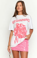 blonde model wearing a white t-shirt with a pink printed rose and the word 'beginning' and a pink sequin skirt in front of a table of rose petals