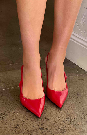 Girl wearing red patent heels with one leg lifted up.