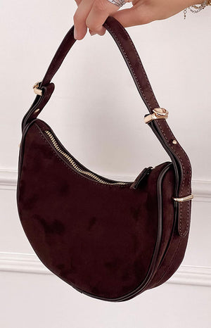 model holding a deep brown faux suede crescent shoulder bag with gold details