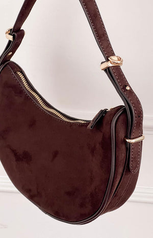 model holding a deep brown faux suede crescent shoulder bag with gold details