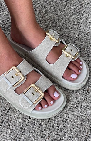 model wearing beige linen sandals with gold buckle details paired with a white shoulder bag