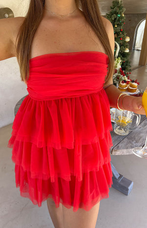 Brunette model wearing a red strapless mini dress with a gold necklace and gold bracelets holding a drink.