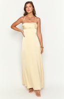 blonde model wearing a yellow satin maxi dress with an open back and strap details holding a white handbag