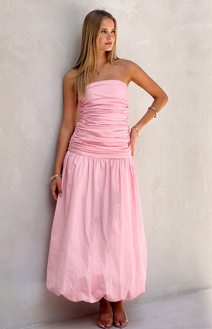 Girl wearing pink maxi dress with clear heels in front of a white wall.