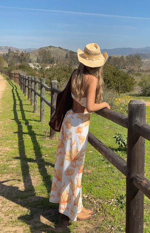 girl is wearing a orange, yellow and white floral strapless maxi dress with side/back cutout detail