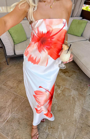 a blonde girl holding a drink stands in a white floral strapless dress and brown heels