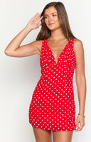 Brunette model wearing a red and white polka dot mini dress with gold jewellery.