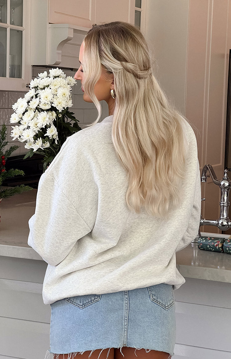 Blonde girl wearing grey sweater and denim mini skirt in front of kitchen sink and white flowers.