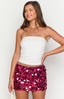 Brunette model wearing a white tank top and hot pink sequin mini skirt with a black handbag and gold jewellery