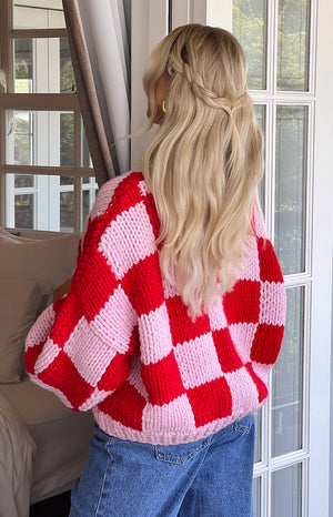 Girl facing away wearing red and pink checkered knit and dark denim jeans. 