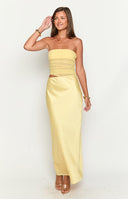 blonde model wearing a yellow mesh and satin maxi dress with gold bracelets and nude sandals