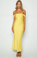 Model with black hair wears off the shoulder yellow maxi dress with nude heels and white beaded necklace.