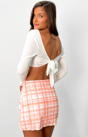 Brunette model wears white knit crop top with tie up back and orange and pink mini skirt.