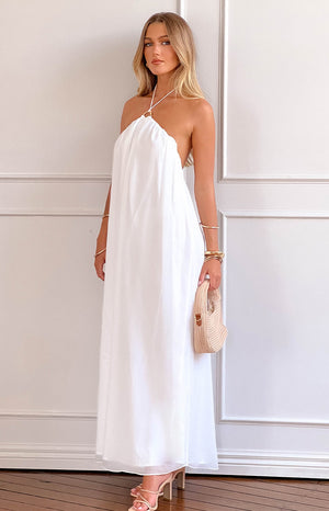 blonde model wearing a white halter neck maxi dress with nude heels and a beige woven handbag