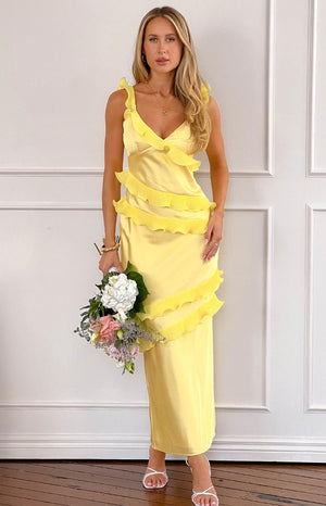 a blonde model wears a yellow maxi dress with ruffles, holding a bouquet of flowers