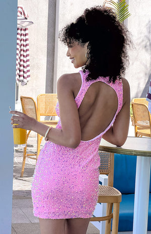 Girl facing away wearing backless pink sequin mini dress in front of outdoor seating area.