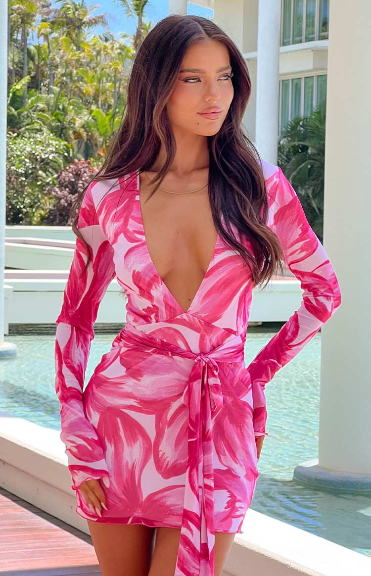 a brunette model wearing a pink floral mini dress with long sleeves posing beside a pool