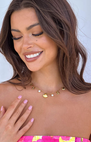 a girl wearing a gold sea shell pendant necklace with pink finger nails smilling