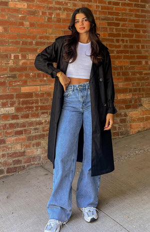 Brunette model is posed front on wearing a black, full length trench coat.