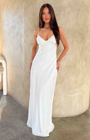 Brunette model wearing white maxi dress in front of cream wall.