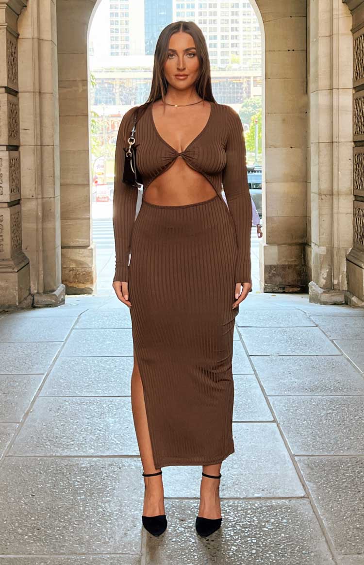 Brunette model wears brown ribbed midi dress with long sleeves and cut out at midriff.