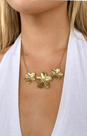 model wearing a gold necklace with three gold pendant flowers and a white top 