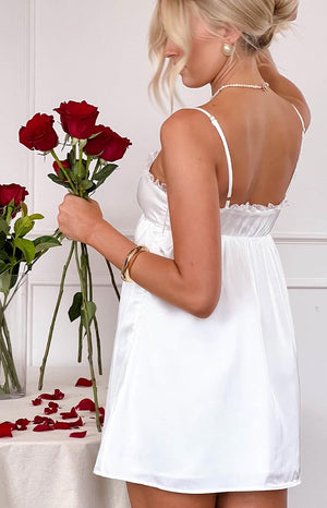 a girl with blonde hair wears a white mini dress holding a bouquet of red roses