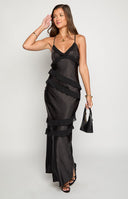 blonde model wearing a black satin formal gown with chiffon ruffle details paired with black heels