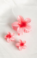 Close up of brunette model with hand holding hair. Her hair is held up by three pink frangipani hair clips. 