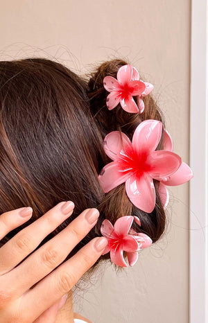 Close up of brunette model with hand holding hair. Her hair is held up by three pink frangipani hair clips. 