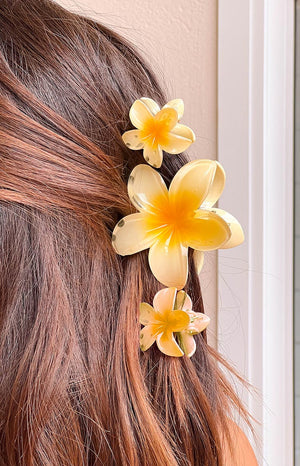 Close up of model with brunette hair, she is wearing three yellow frangipani hair clips in her hair to hold it back. 