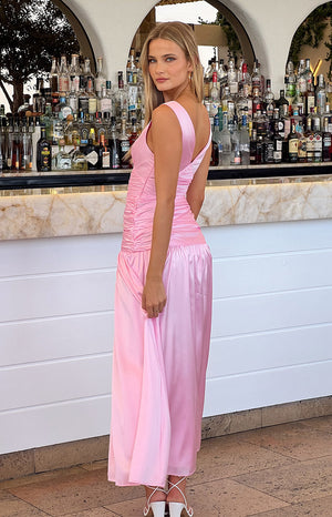 Girl wearing pink maxi dress and white heels in front of a bar. 