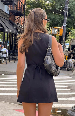 Girl facing away wearing black mini dress and black shoulder bag. 