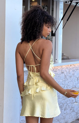 Girl facing away wearing yellow frill mini dress holding a cocktail glass. 